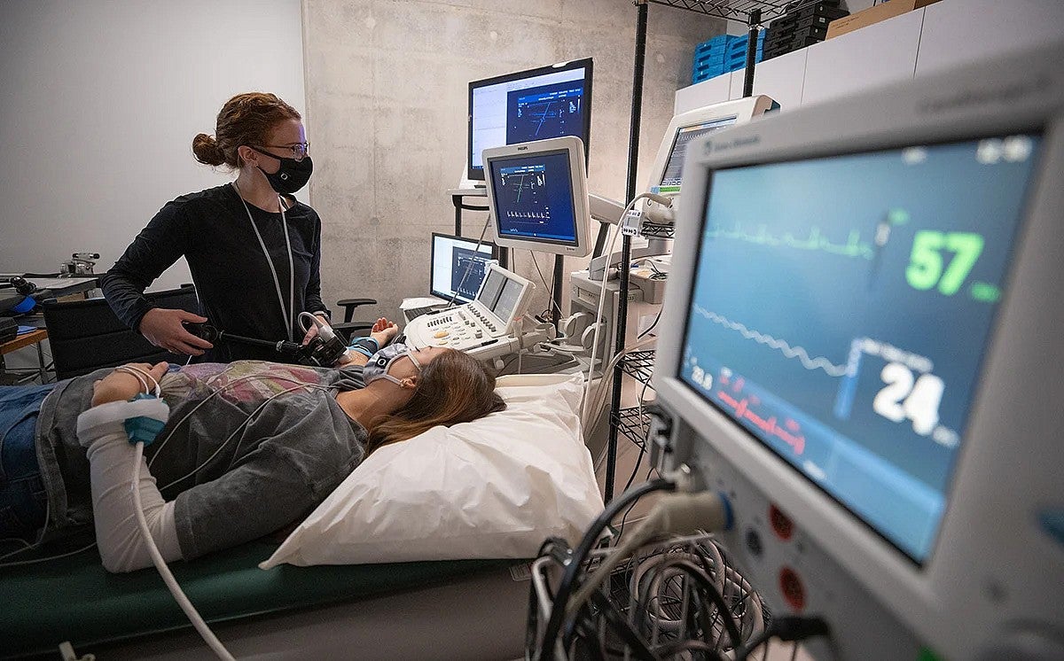 A person laying on a bed with a researcher standing next to them looking at monitors