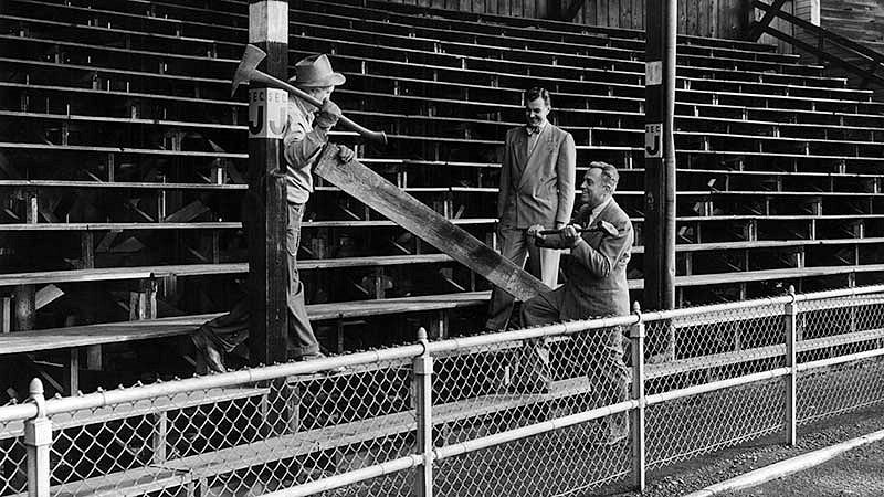 Three men, including University of Oregon athletic director Leo Harris (holding the sledge hammer) posing for a commemorative shot as work to remove the north bleachers at Hayward Field is set to begin in 1950.