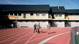 Former track coach Bill Bowerman and two other men walking on the Hayward Field track, away from camera towards the Bowerman Building 